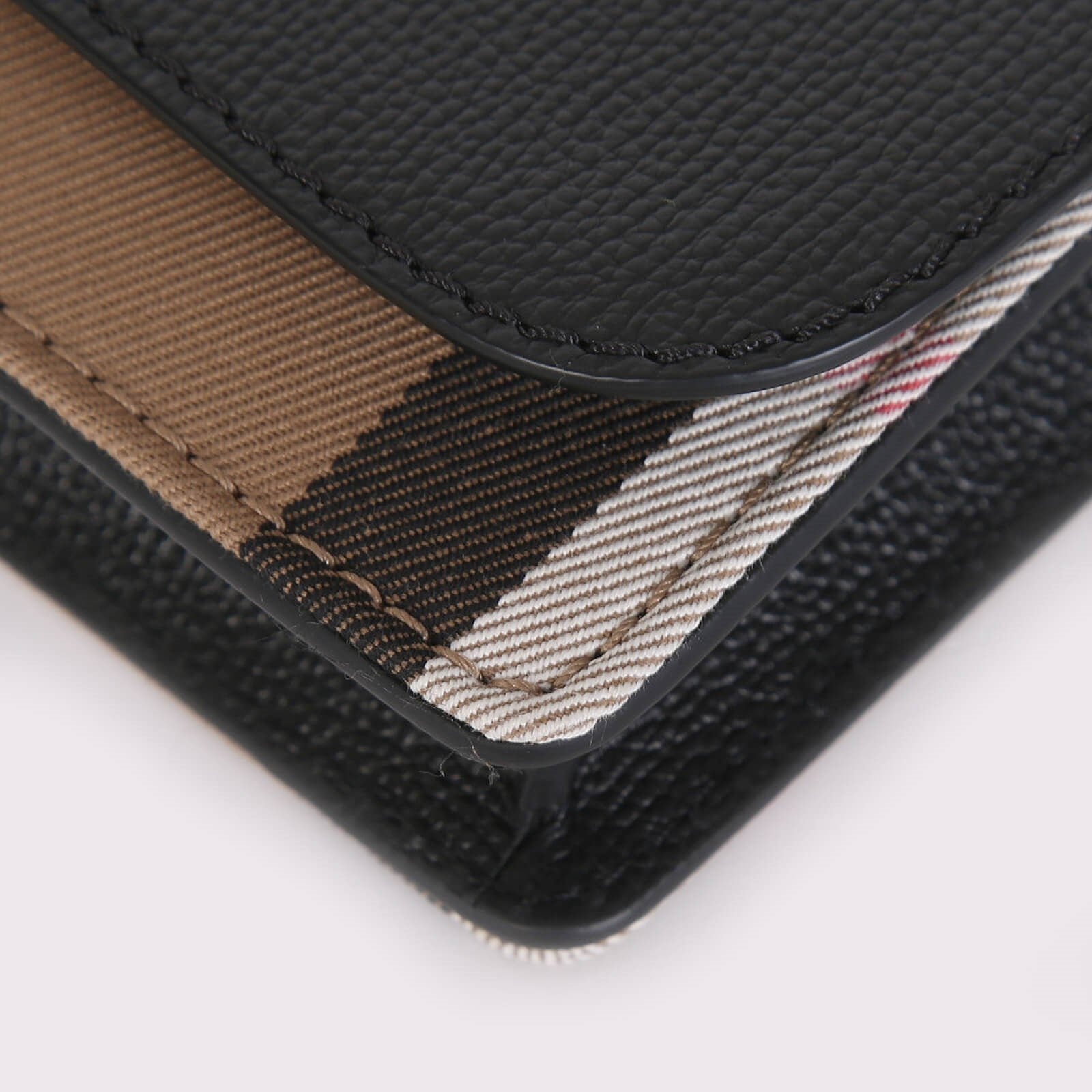 Close-up detail of Burberry crossbody bag black showing textured leather and signature check fabric