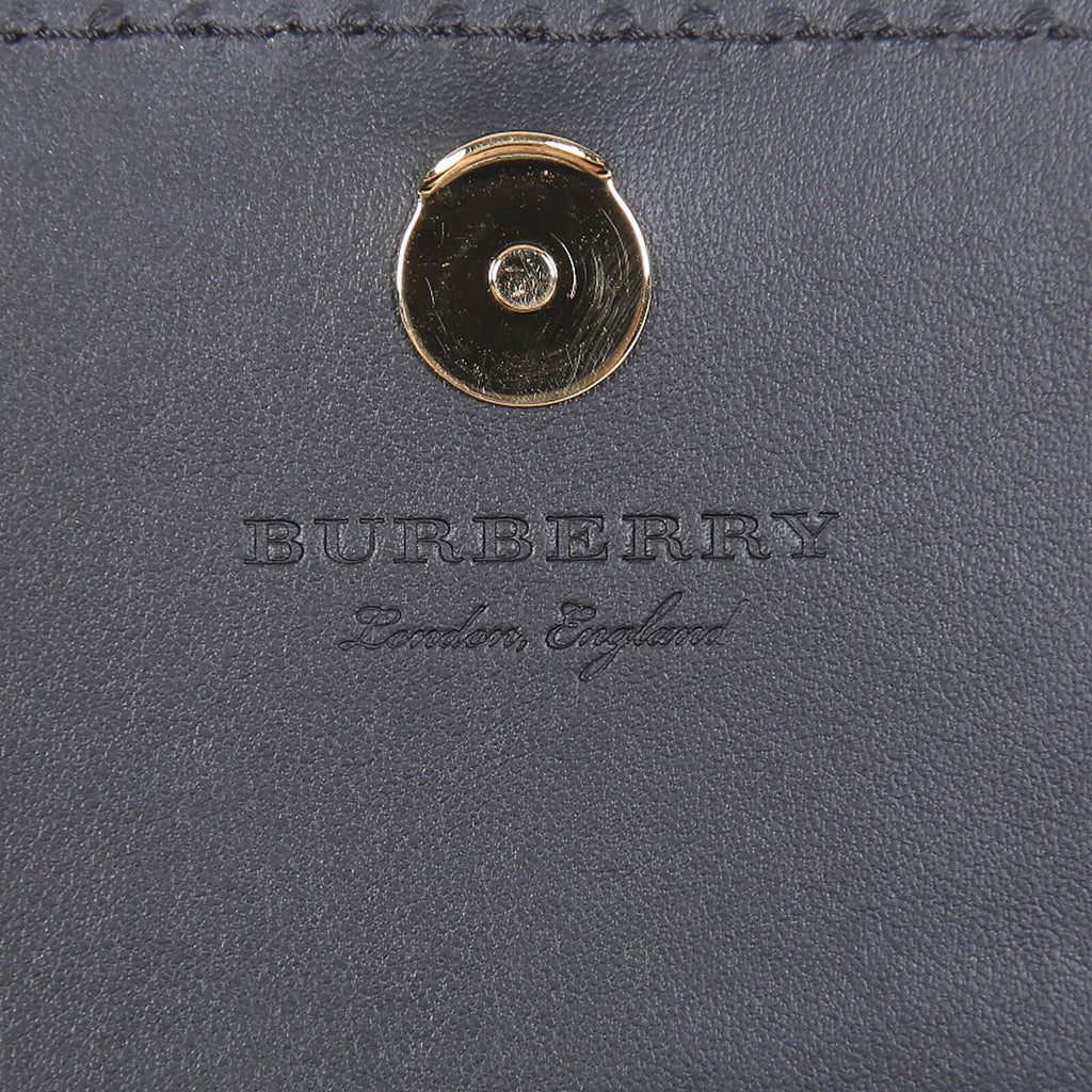 Close-up of Burberry crossbody bag black leather with gold button clasp and embossed logo