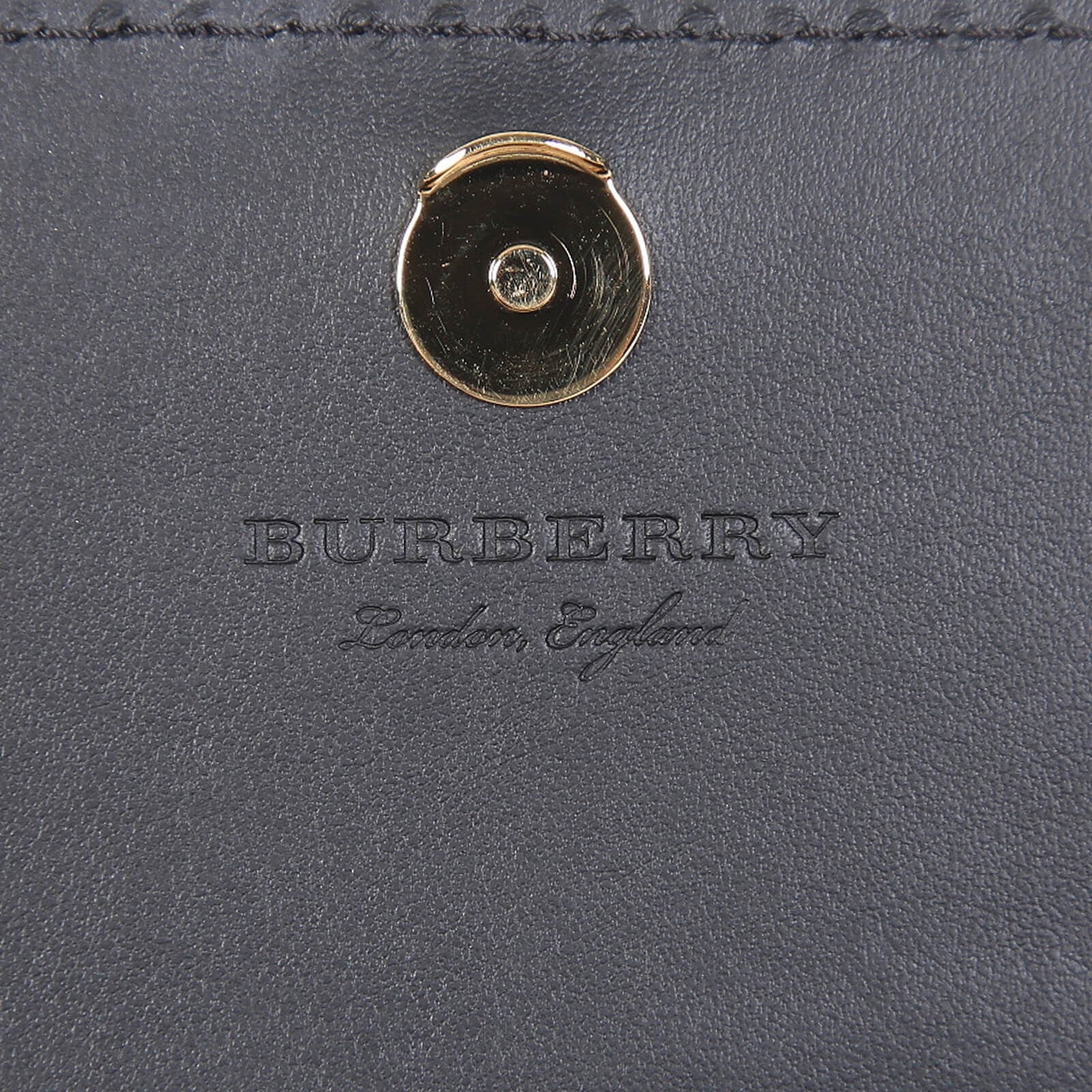 Close-up of Burberry crossbody bag black leather with gold button clasp and embossed logo